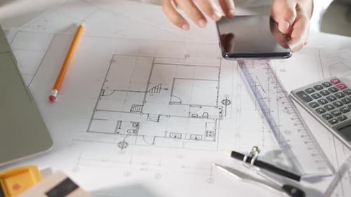 Architect Working on Plans with Phone and Pencil