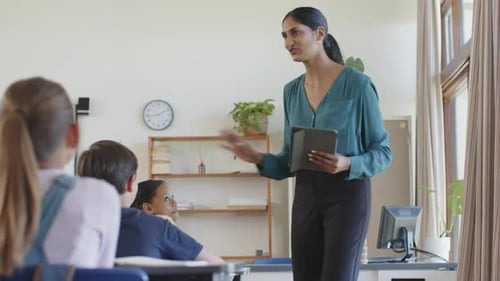 In school, teacher holding tablet and engaging with students in classroom