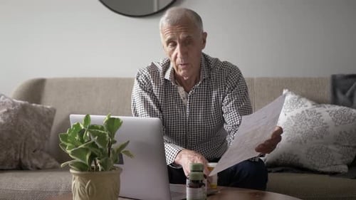 Senior Man Discussing Medication With Doctor By Video Chat On Sofa Slow Motion