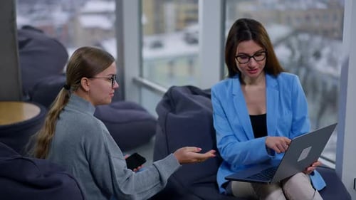 Female colleagues sitting close in bean bag chairs talking about work.