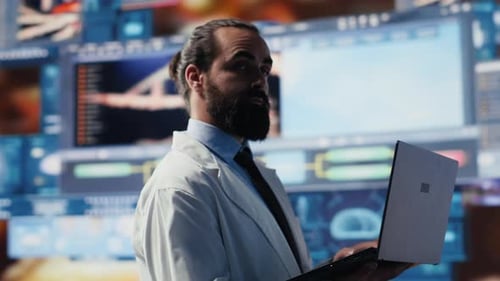 Man in Lab Coat Uses Laptop with Medical Data