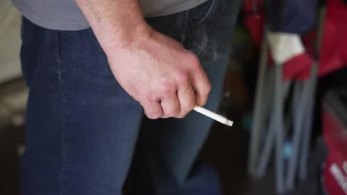 Nahaufnahme einer kaukasischen Männerhand, die eine brennende Zigarette hält.