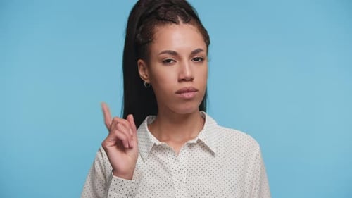 Ernsthafte Frau warnt mit erhobenem Finger auf blauem Hintergrund