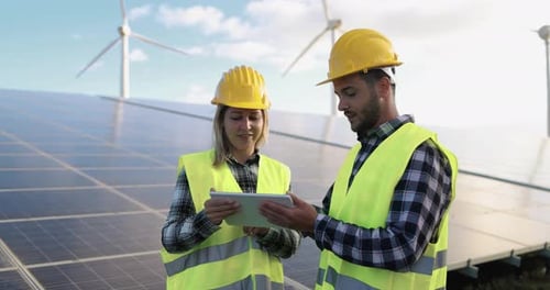Junge Leute arbeiten mit digitalem Tablet an Solarzellenstation und Wind