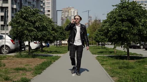 A Business Man in a Leather Jacket and Plaid Trousers Walks to a Residential Area Talking on the