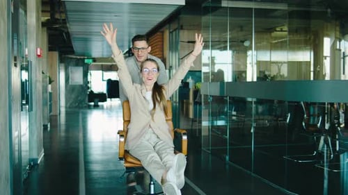 A Joyful Moment in the Office As a Team Member Pushes a Colleague on a Chair Highlighting a Fun and