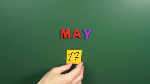 Hand sticking a sticker 17 May calendar day on school board. 17 date of May. Seventeenth day May