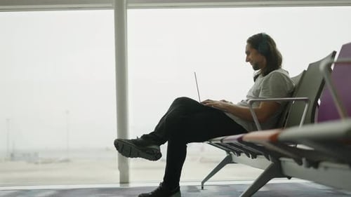 Adult Digital Nomad Man Looking at the Camera and Smiling While Using His Laptop Sit on an Airport
