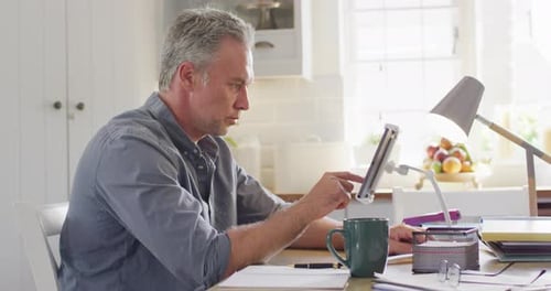 Man Works at Desk Using Tablet at Home