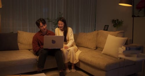 Young Couple Relaxing on Couch with Laptop at Night