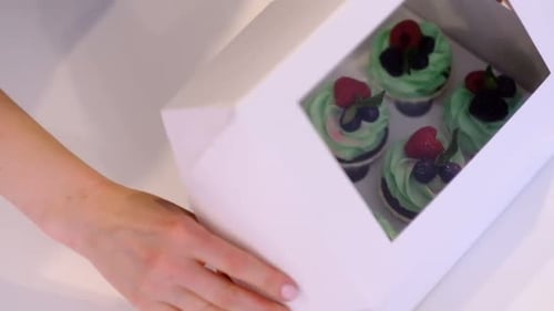 Hands of Female Pastry Chef Packaging Freshly Made Cupcakes with Buttercream Frosting Into Gift Box