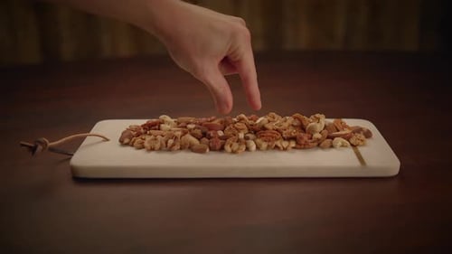 Hand Picks Walnut from Wooden Board with Nuts