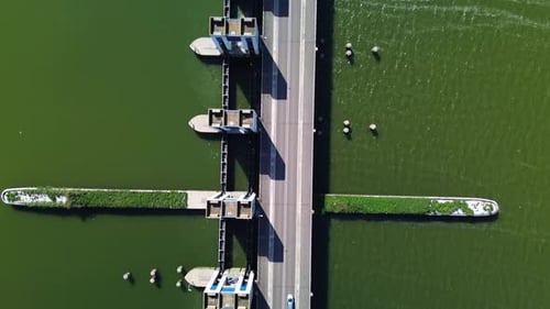 Vue aérienne d'un barrage maritime avec des piliers en béton, contrôlant le débit d'eau entre la mer et l'intérieur des terres