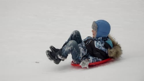Young boy sledding down a snowy hill in slow motion. This clip captures the excitement