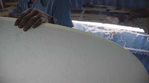 Asiatischer Mann von Slowmo, der in der Werkstatt an einem DIY-Surfschaumbrett arbeitet. Schnittlinie zeichnen