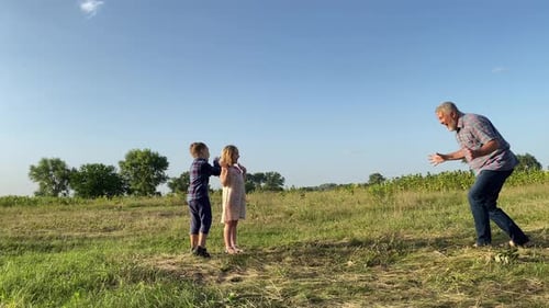 Grandfather Plays Tag with Grandchildren in Grassy Field