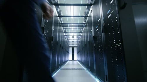 Un ingeniero de servidores entra por las puertas corredizas que se abren y atraviesa el pasillo del centro de datos. Set de trabajo