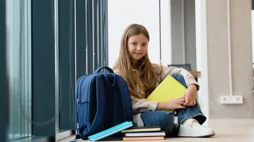 Porträt einer Schülerin mit einem Buch, das im Klassenzimmer auf dem Boden sitzt Zurück zur Schule