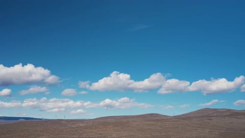 White puffy clouds slowly move across bare empty desert hills, aerial track