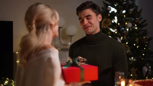 Rear View of Happy Surprised Young Woman Receiving Christmas Gift From Loving Man at Home on