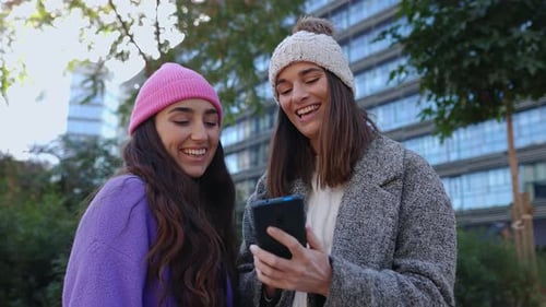 Two Young Women Enjoying Phone in Urban Park