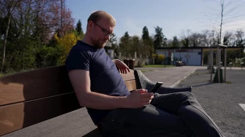 Man Using Phone While Sitting on Park Bench