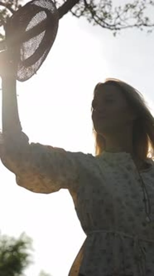 Woman puts on sun hat in nature setting