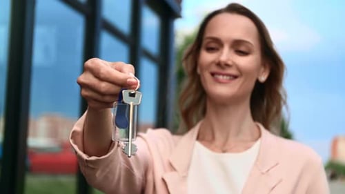 Woman Holds Keys Outside Apartment Building Smiling