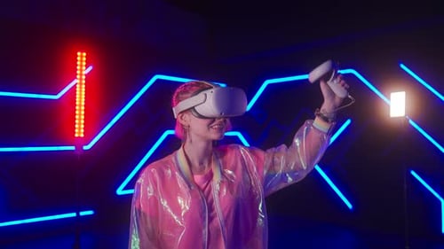 Young Female Gamer in Pink is Playing Virtual Reality Games VR Headset and Controllers
