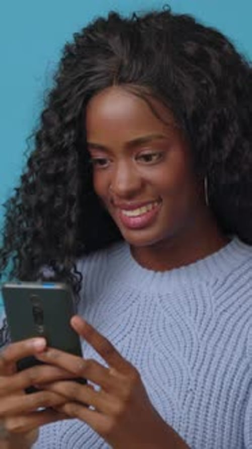 Happy Young Latin African Woman Using Mobile Phone Over Blue Background
