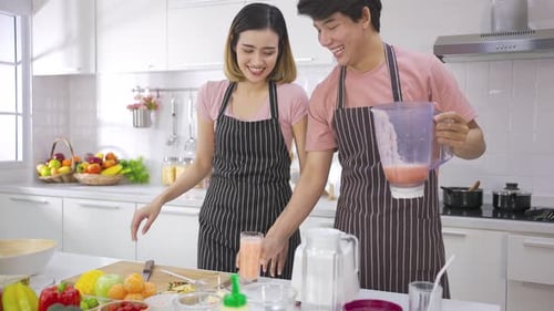 Pareja de jóvenes asiáticos preparando vegetarianos, bebiendo un batido fresco y sonriendo, disfrutando