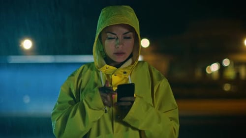 Woman in Yellow Raincoat Using Phone at Night
