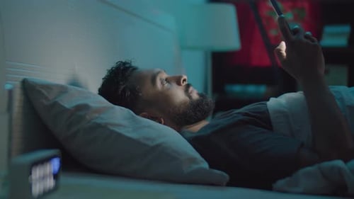 Man Lies in Bed Looking at Mobile Device