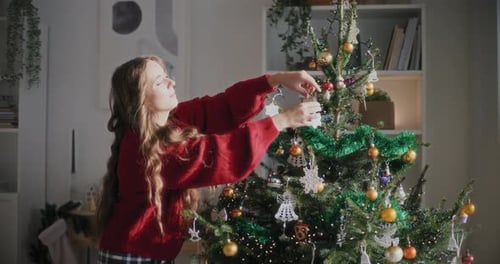 Woman Decorating Christmas Tree With Ornaments Indoors
