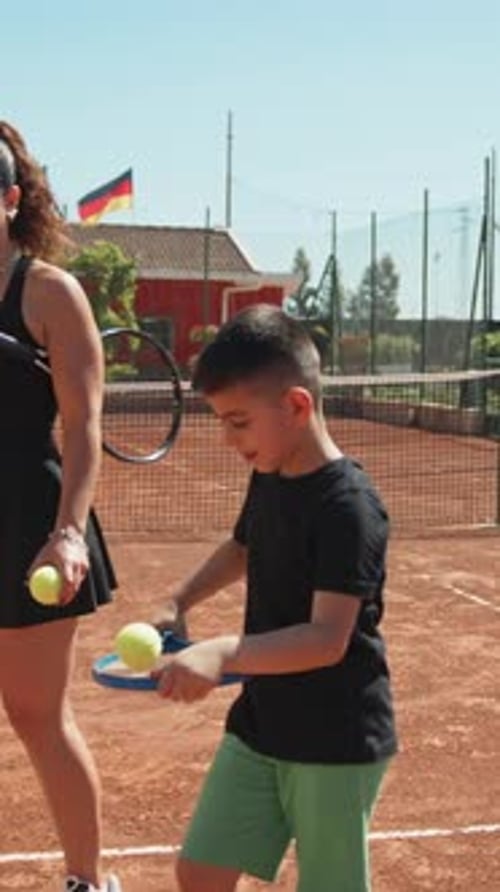 Woman Teaching Boy Tennis on Clay Court