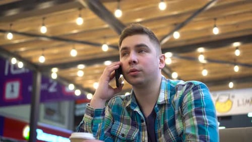 A Young Man is Sitting in a Cafe and Talking on the Phone