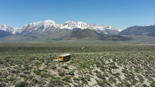 Yellow school bus travels across the remote desert with snowy Sierra Nevada mountains in the backgro