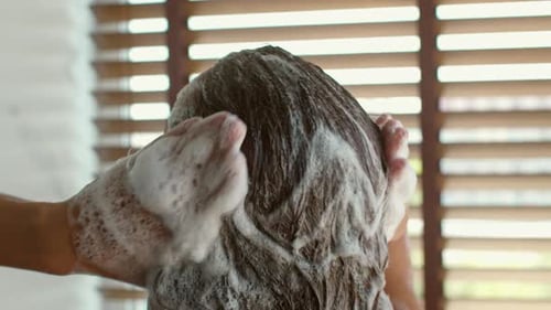 Woman Massaging Shampoo Into Hair in Bright Shower