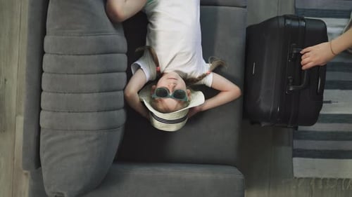 Girl Lying on Couch with Suitcase Passing By