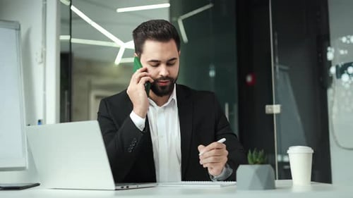 Employer Making Notes While Having Phone Call and Sitting in Contemporary Office