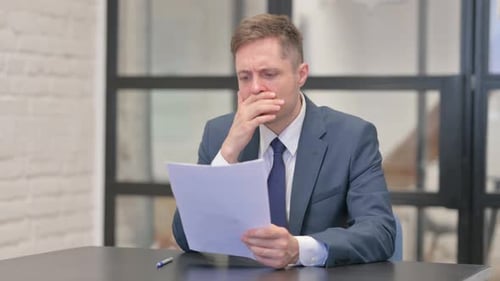 Concerned Businessman Reviews Document at Office Desk