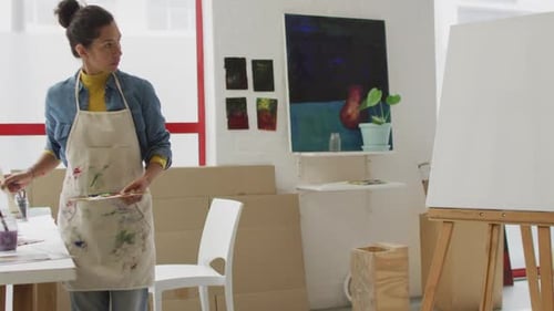 Video of biracial female artist painting in studio