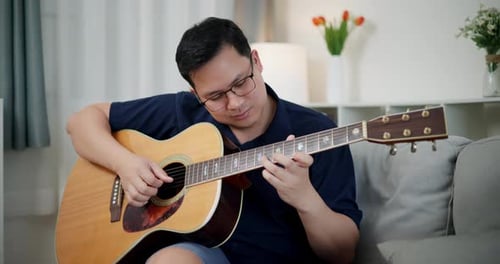 Man Plays Acoustic Guitar on Couch Indoors