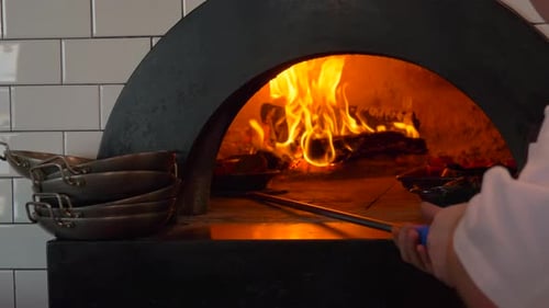 Chef Placing Dishes in Wood Burning Pizza Oven