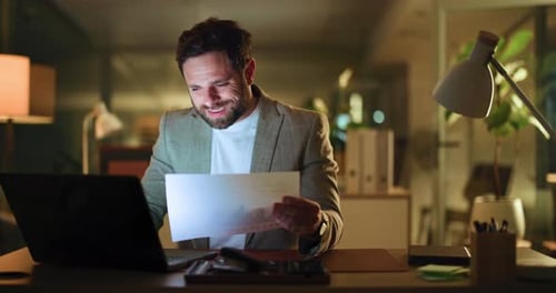Man Works Late on Laptop with Paperwork