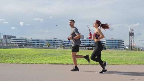 Slow Motion A Fit Couple Jogging Together Outdoors on a Grassy Field Showcasing Teamwork Fitness