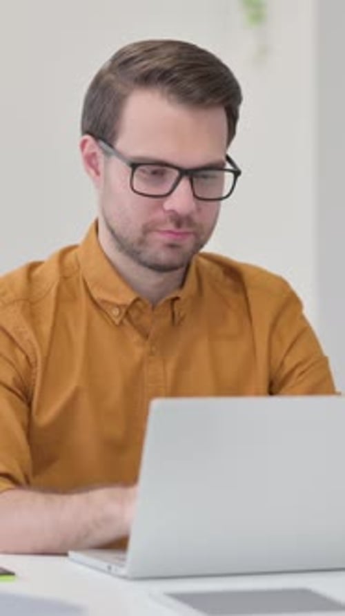 Man Typing on Laptop, Smiling at Camera in Office