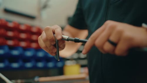 Golf club builder's hands twist iron head onto golf club shaft and secure for custom build in worksh