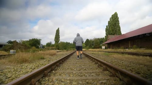 Back View Of A Sporty Man Running On Empty Railroad. following shot