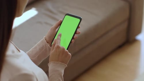 Over Shoulder View of Young Lady Watching Show on Smartphone with Green Chroma Key Screen Empty